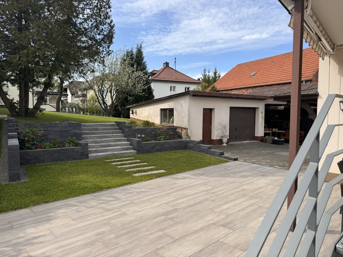 Ein gepflegter Garten mit Rasen, Steintreppen und blühenden Pflanzen.