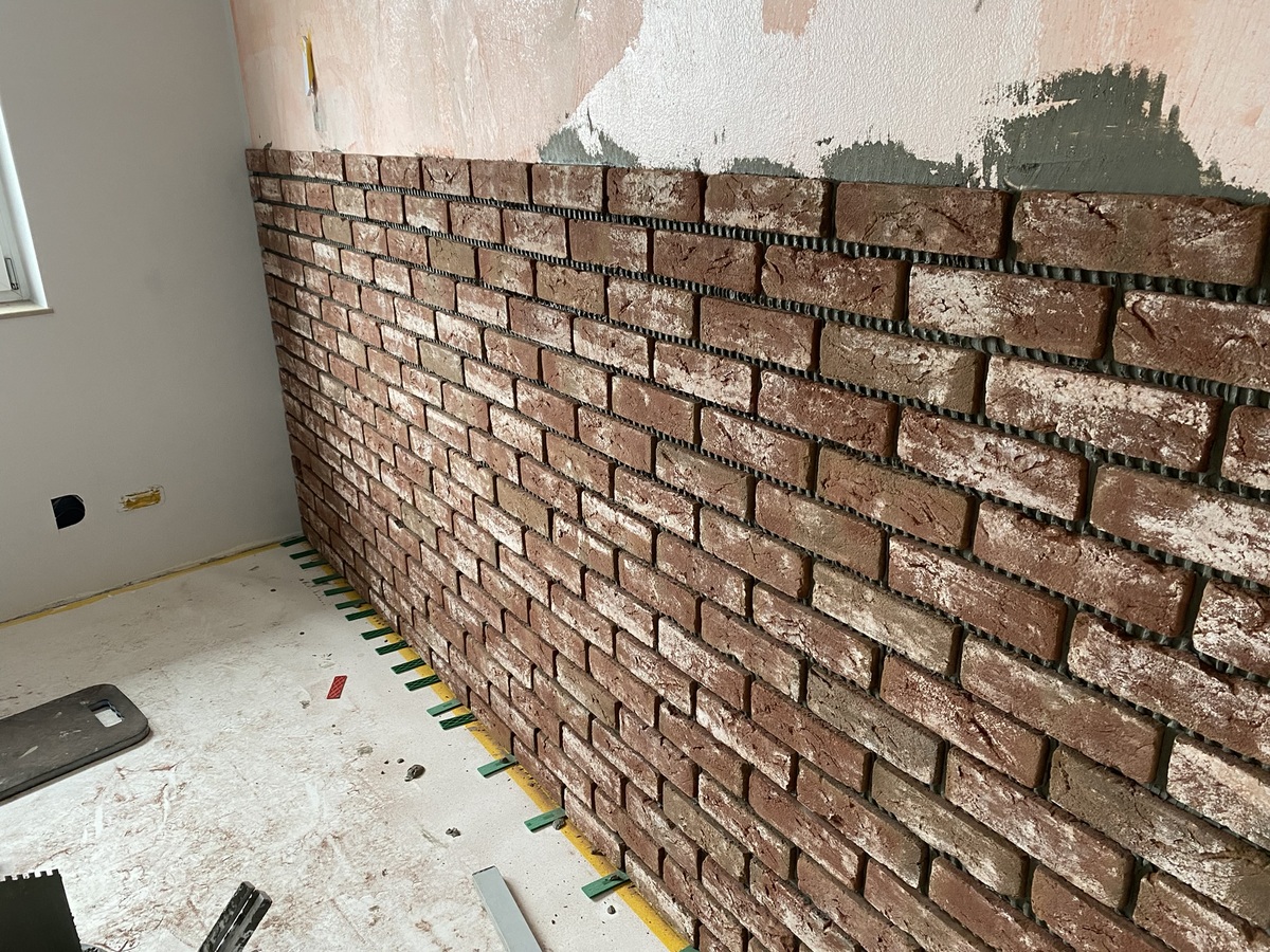 Grober Ziegelmauerbau in einem Raum, die obere Wand ist noch verputzt.