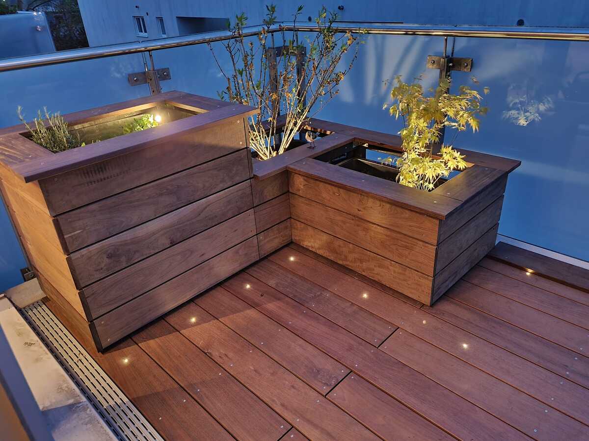 Holzterrasse mit Pflanzenkästen und stimmungsvoller Beleuchtung bei Abenddämmerung