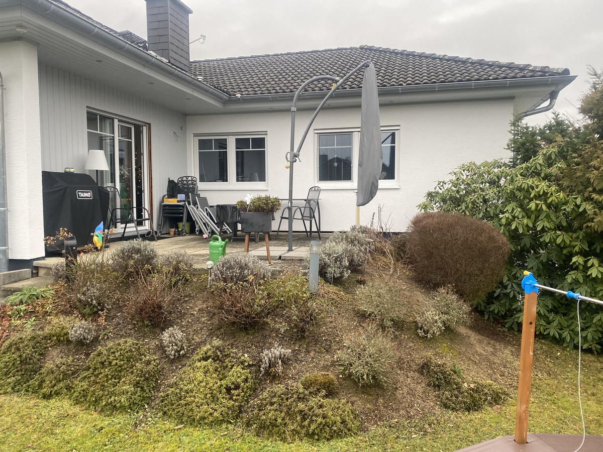 Ein Haus mit weißer Fassade, schiefergrauem Dach und schönem Gartenumgebung.