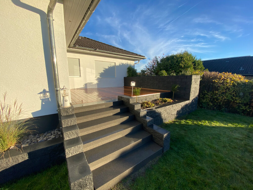 Treppe aus grauem Stein führt zur Terrasse eines weißen Hauses bei Sonnenschein