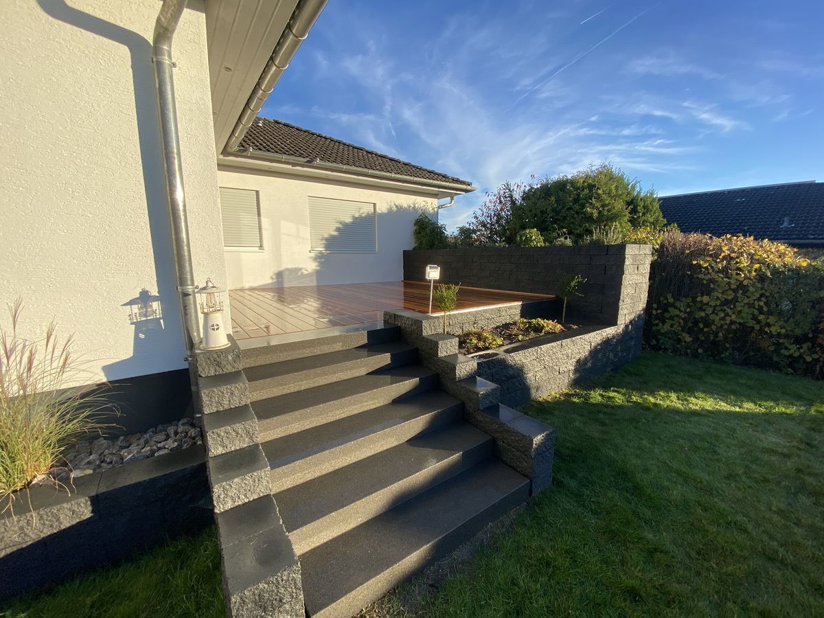 Sonniger Garten mit Steintreppe und Terrasse, umgeben von grünen Pflanzen.