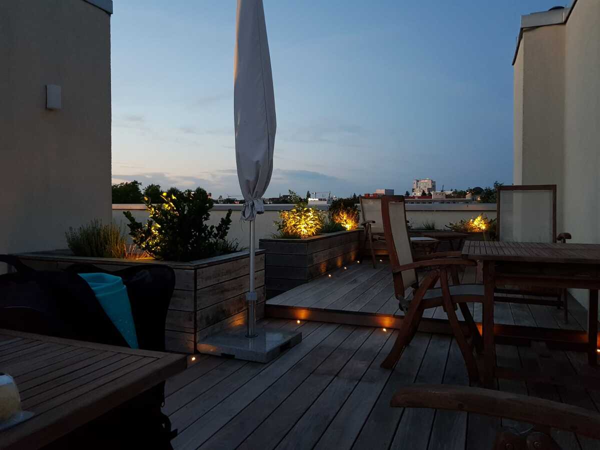 Eine ruhige Dachterrasse mit Holzbelag, stimmungsvoller Beleuchtung und Pflanzen.