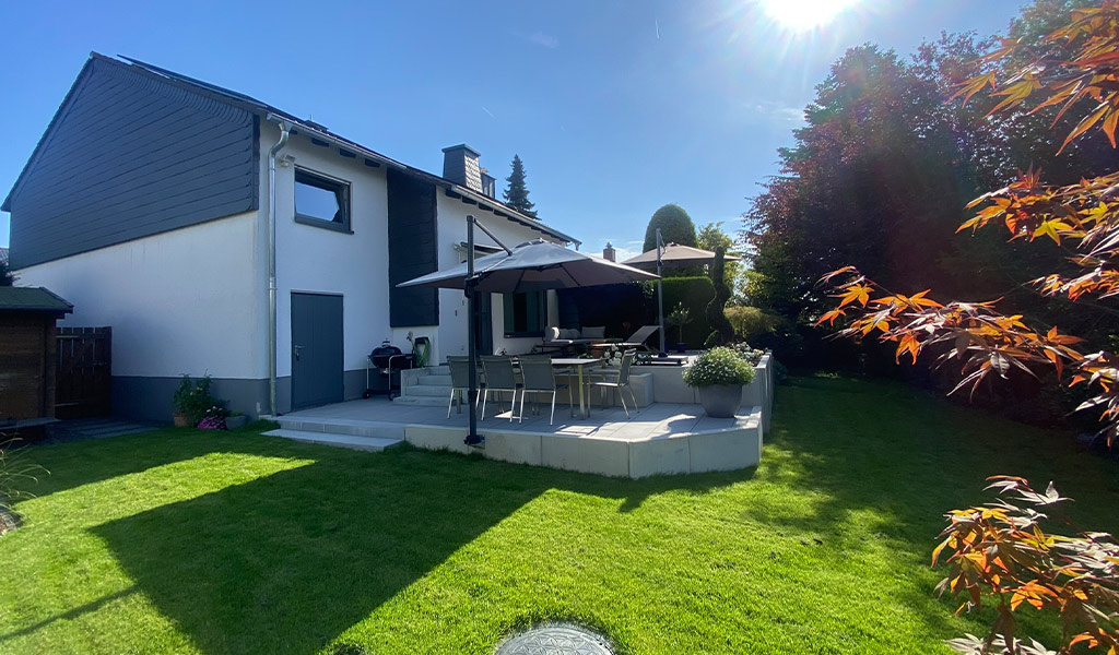 Ein modernes Einfamilienhaus mit grauen Akzenten und einem gepflegten Garten im Sonnenlicht.