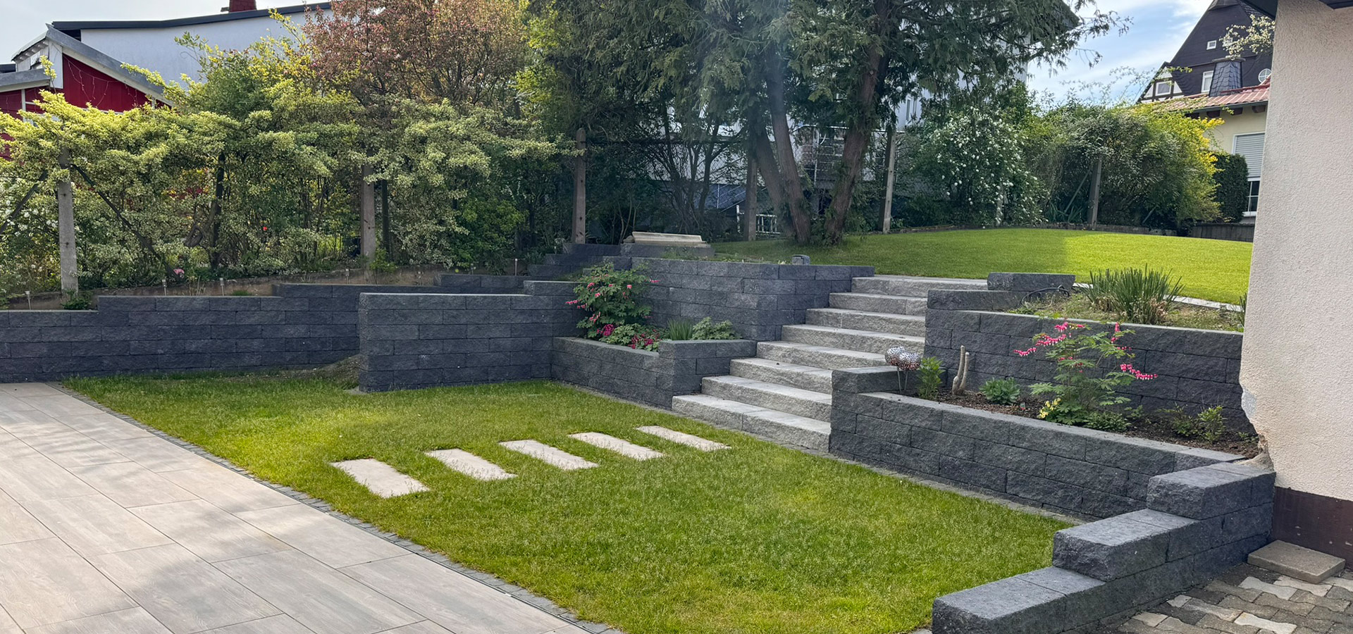 Ein gepflegter Garten mit modernen grauen Steinmauern und Stufen in der Sonne.
