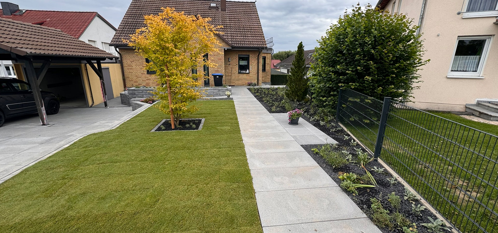 Ein gepflegter Garten mit grünem Rasen, einem schönen Baum und Blumen.