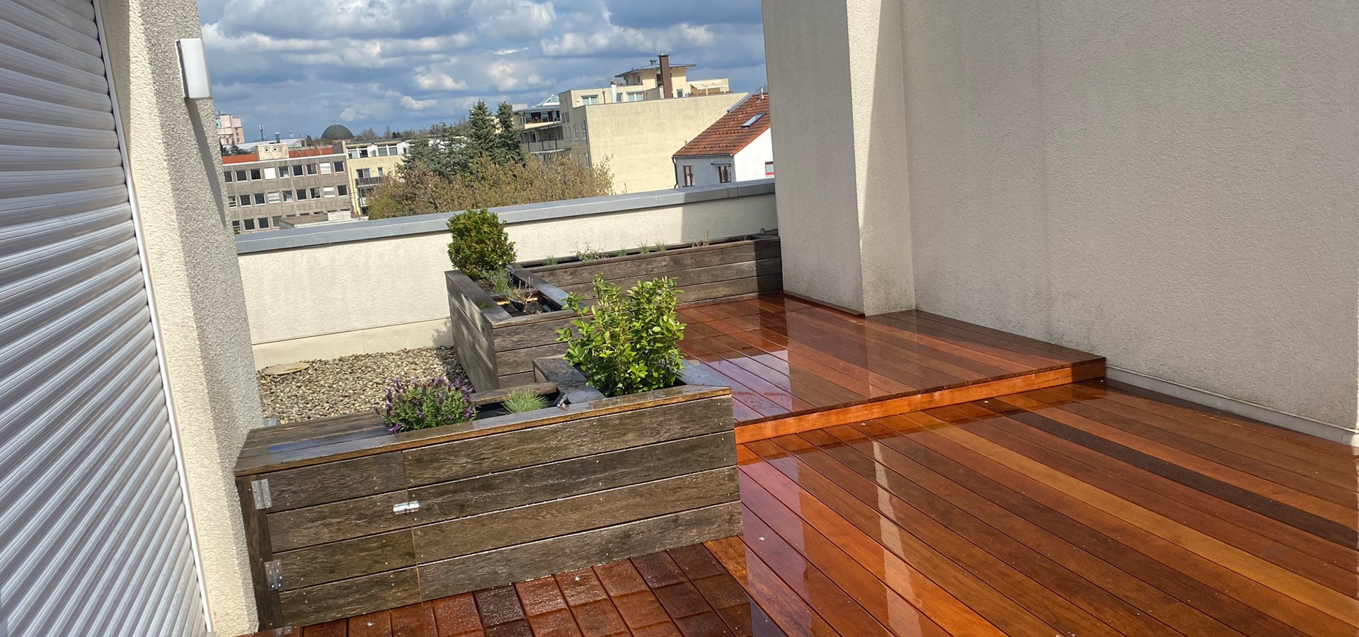 Eine moderne Holzterrasse mit Pflanzenkästen und Wolken am Himmel.