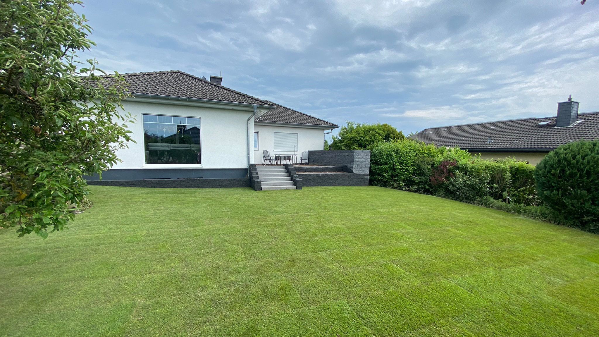 Ein weißes Einfamilienhaus mit gepflegtem Rasen und bewölktem Himmel