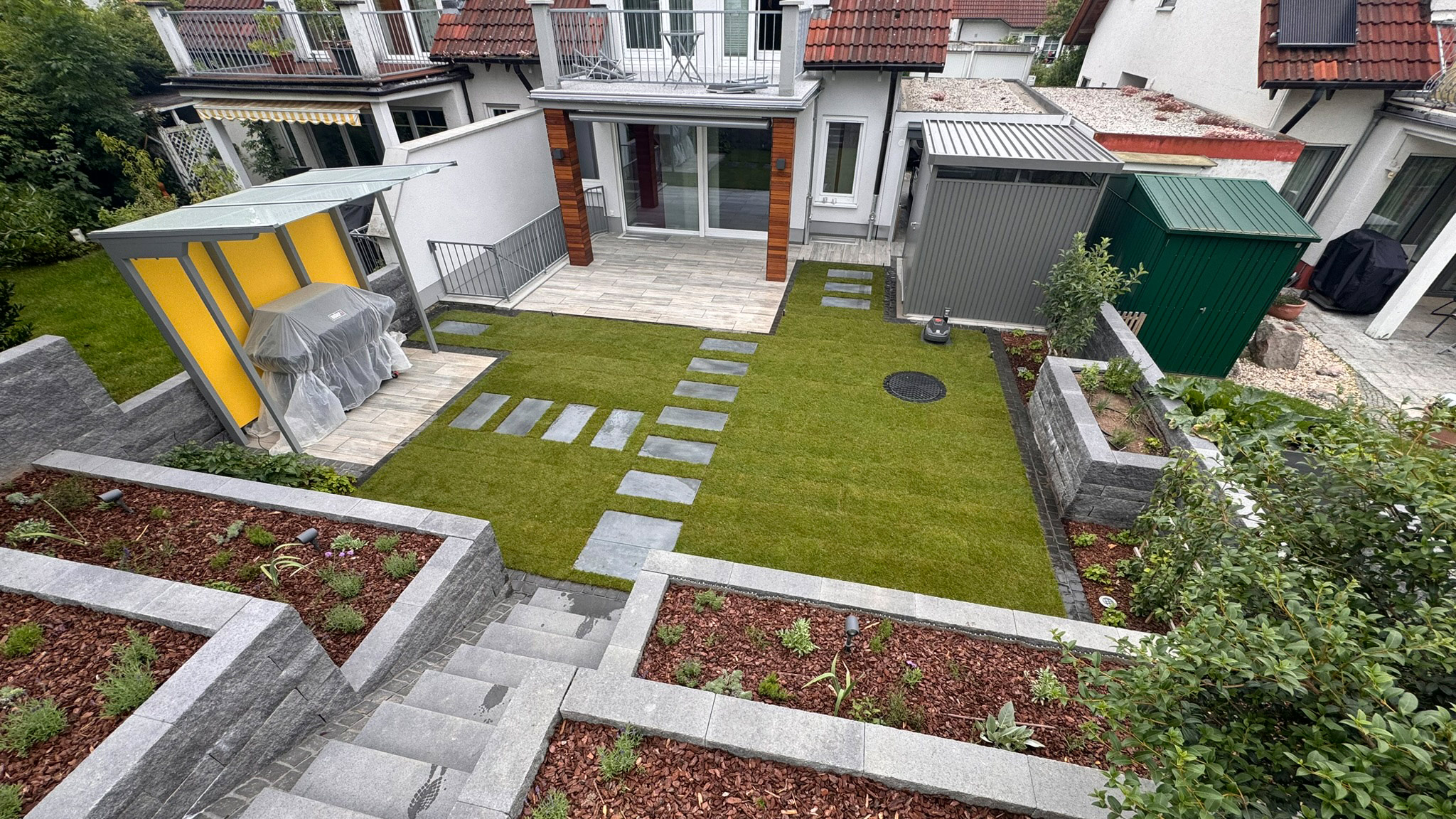 Ein moderner Garten mit frischem Rasen, Steinpfad und bepflanzten Blumenbeeten.